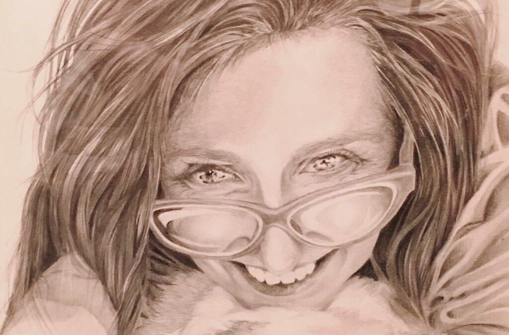 Female artist self portrait. It’s close up and she is looking over the top of her glasses smiling at something