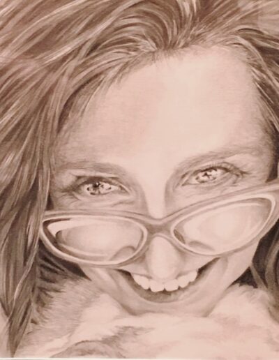 Female artist self portrait. It’s close up and she is looking over the top of her glasses smiling at something