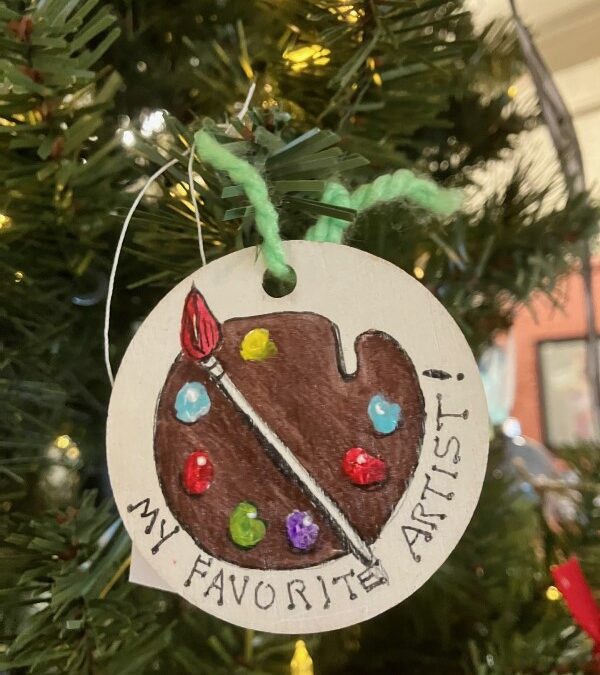 picture of hand painted ornament stating My Favorite Artist! featuring a brown palette with various dabs of colored paint and a paintbrush